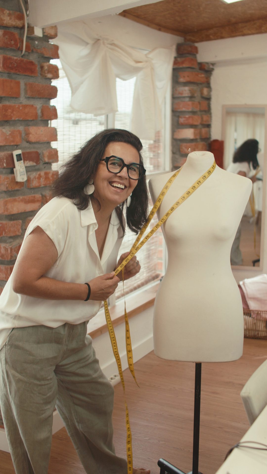 Helena, fundadora do Argolinhas, com uma fita métrica junto a um manequim no atelier
